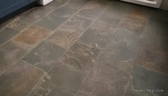 Dull riven slate floor in a UK kitchen depicting residue trapped in grout joints and flat grey surface prior to cleaning